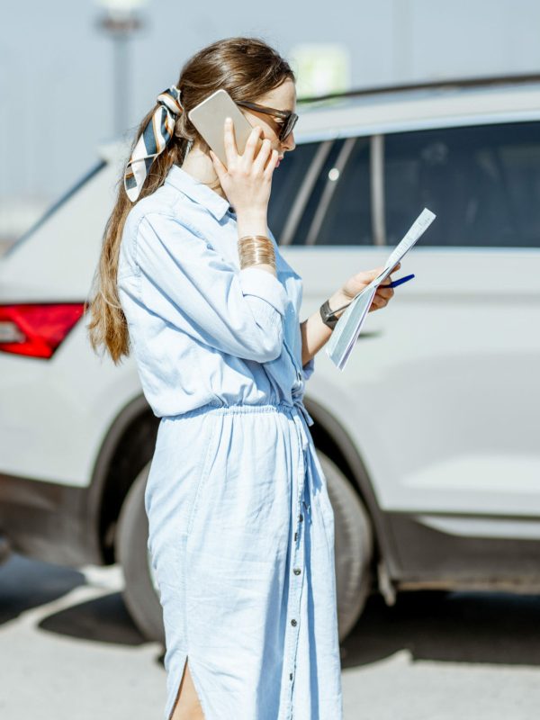 Woman calling with phone after the car collision Woman calling road assistance or insurance company standing on the road after the car collision, man checking the damage